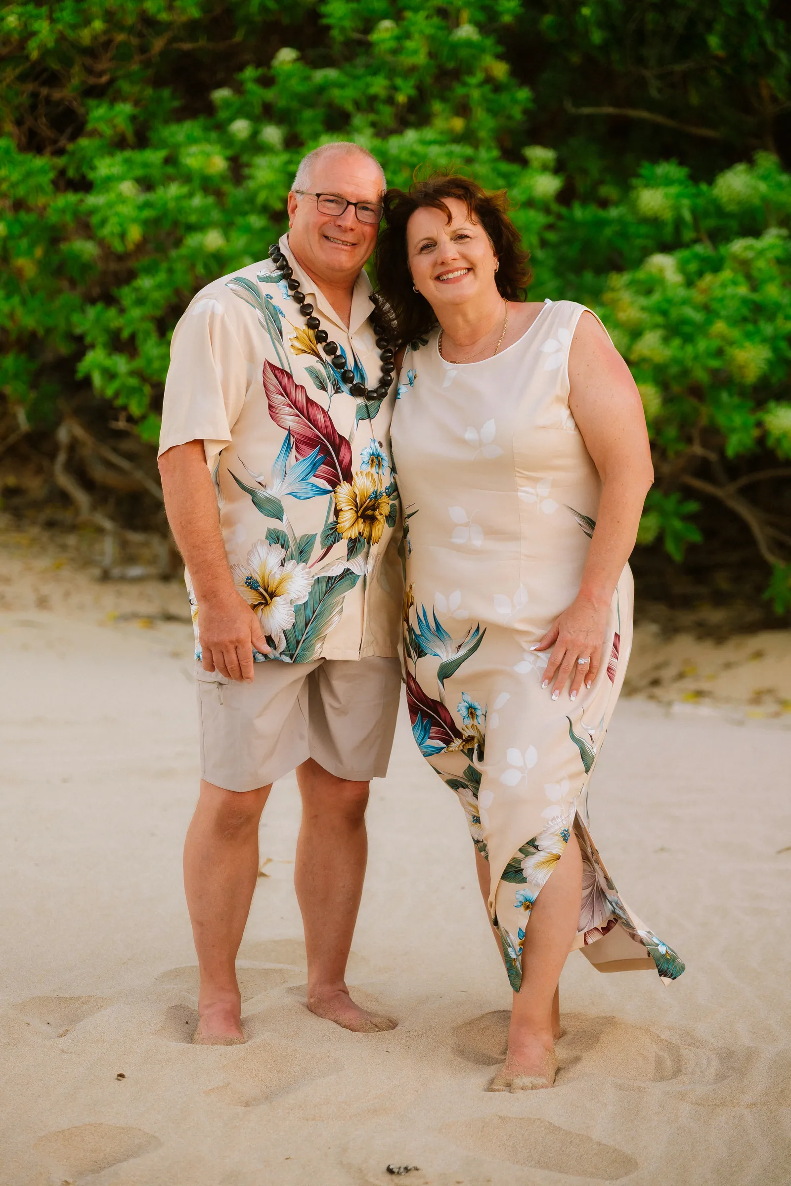 A couple in aloha wear photographed against dense green foliage