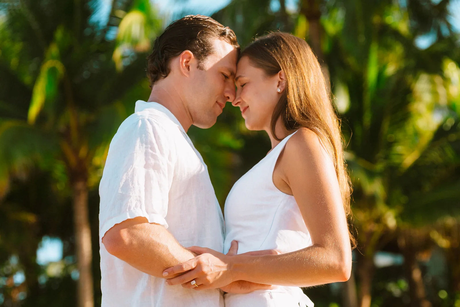A couple forehead to forehead beneath palms in soft afternoon light