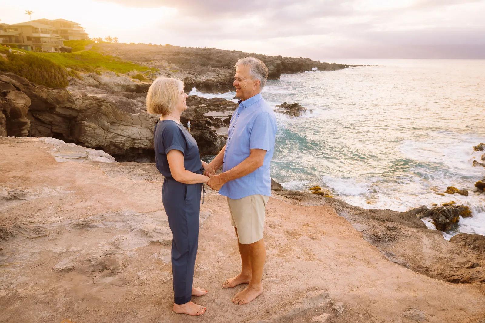 A couple holding hands on a rocky coastline, the shore curving away behind them