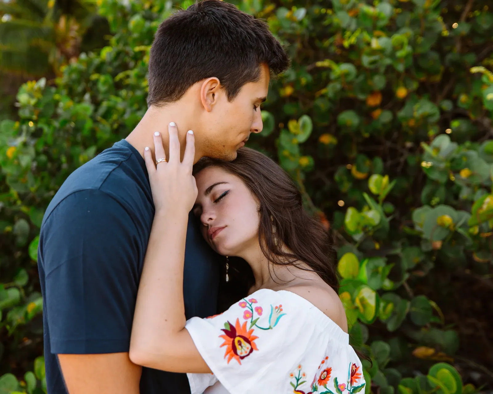 Engaged couple holding each other under coastal foliage on Maui's south shore