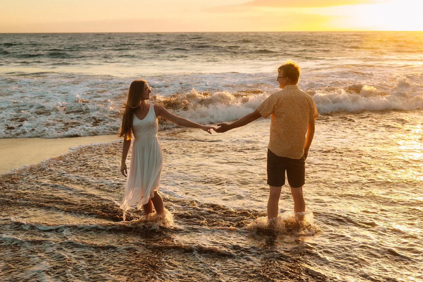 A couple walking hand in hand through ankle-deep water at sunset