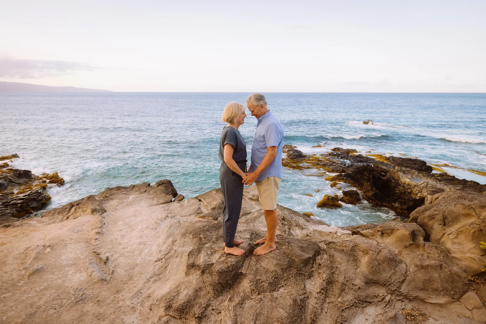 A couple embracing on weathered lava rock with the ocean beyond