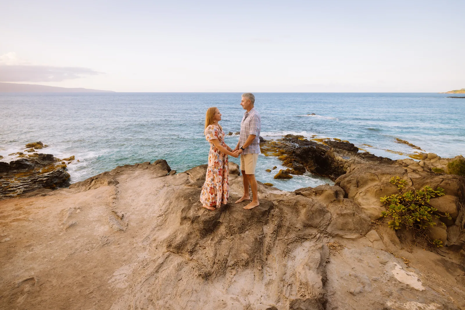 A couple holding hands on a lava shelf above the water