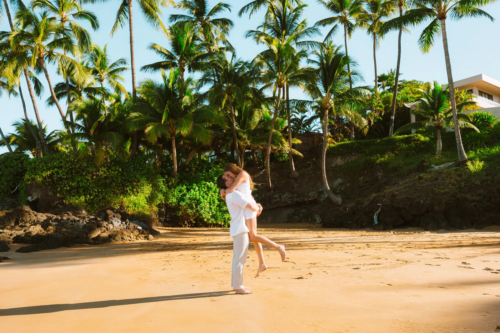 A wide view of a palm-backed cove with a couple walking the sand