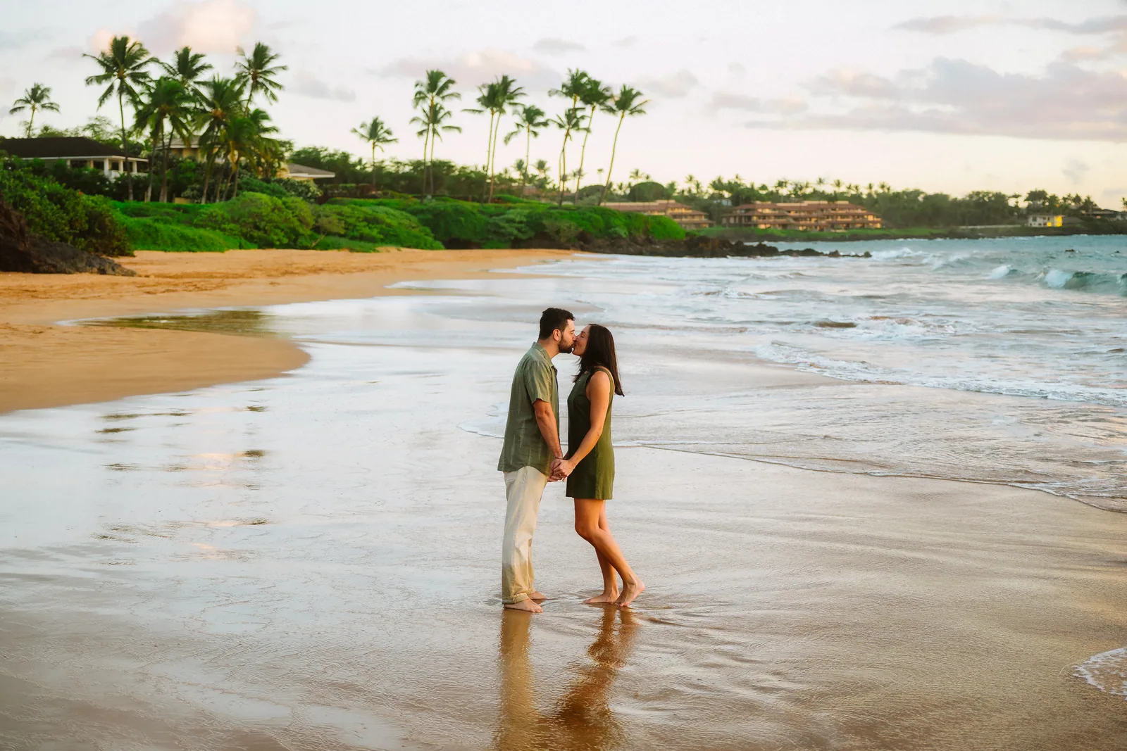 A couple facing each other on wet sand, reflected in the shallow water