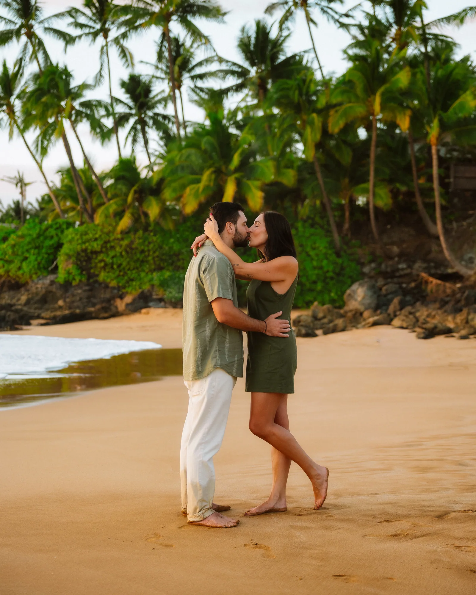 A couple embracing on the sand with a green headland rising behind them
