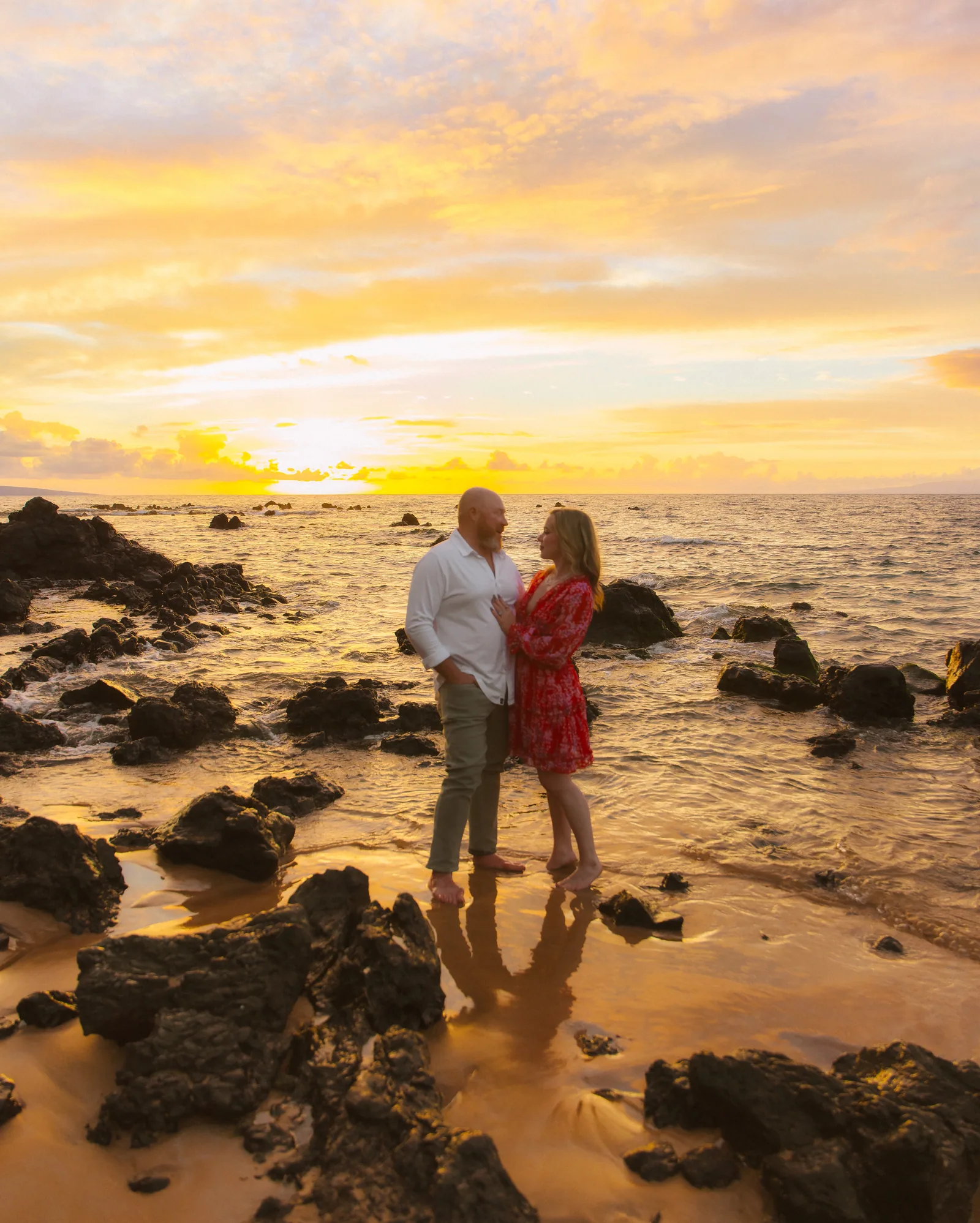 A couple standing together among rocks under a broad sunset sky