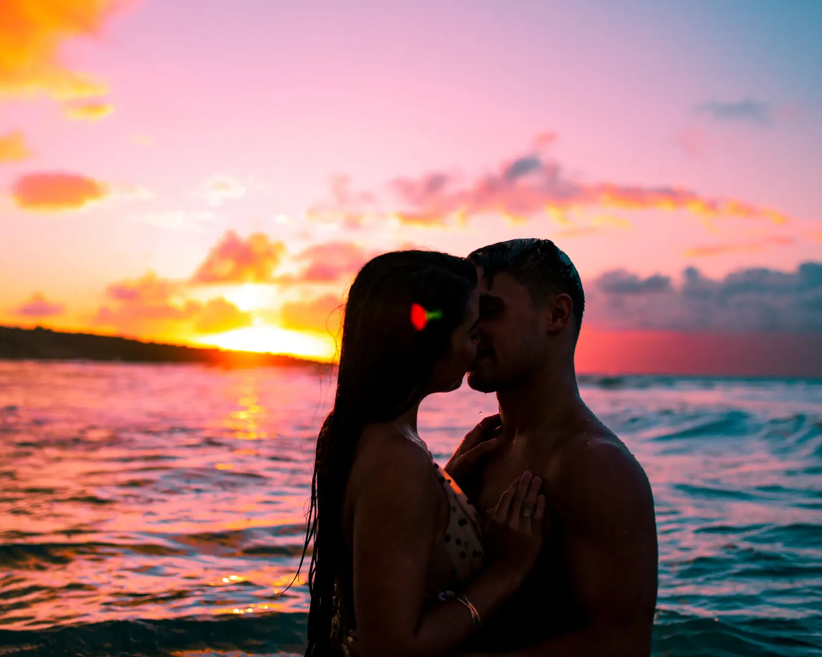 Couple standing in the ocean silhouetted by a burning Maui sunset