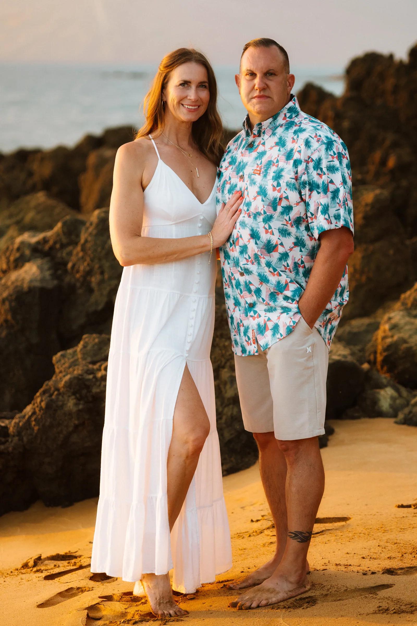 A couple photographed beside dark lava rock, her white dress bright against it