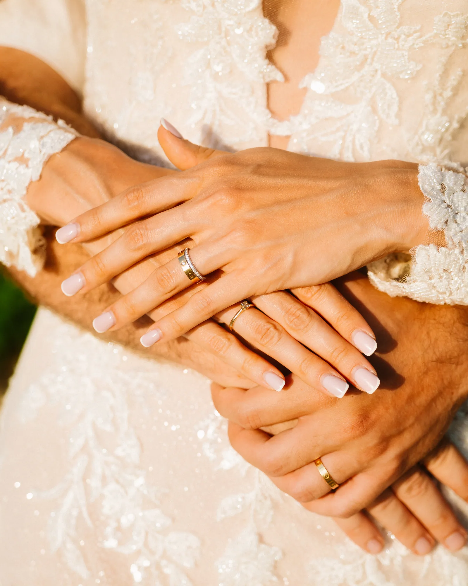 Hands resting together against the lace of a wedding gown