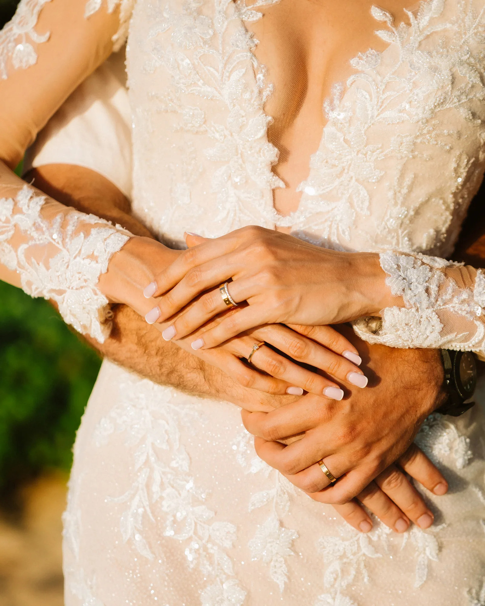 Both wedding bands visible as hands rest at the waist of a lace gown