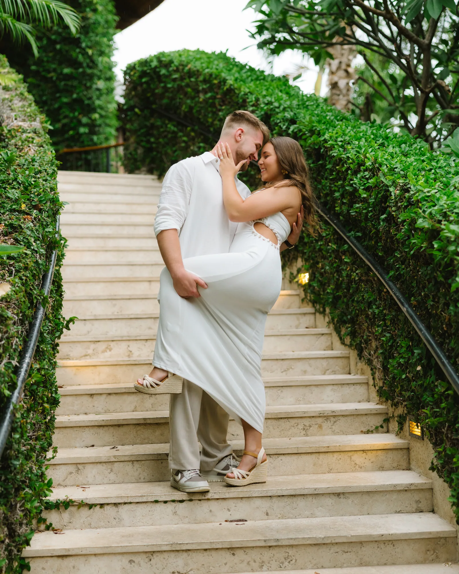 A couple in white mid dip-kiss on a garden staircase