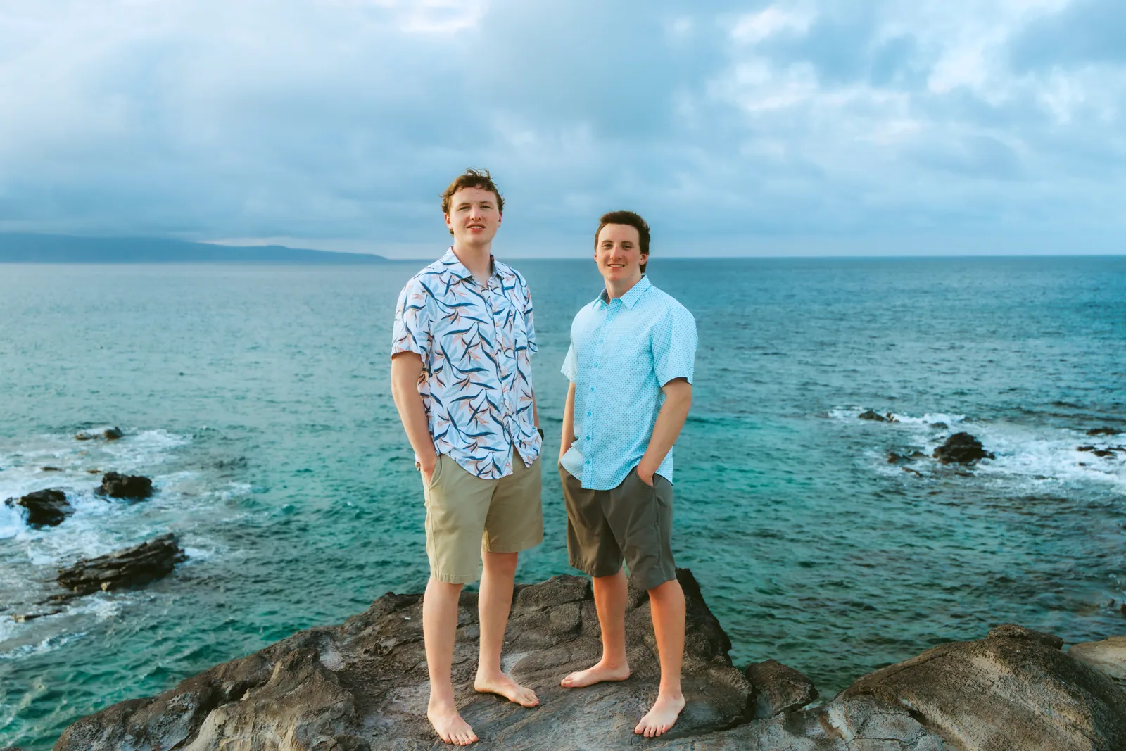 Two brothers standing on lava rock above a turquoise cove
