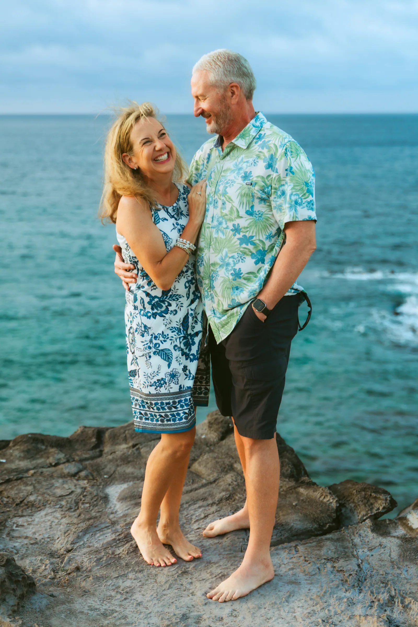 A couple in aloha wear photographed on the rocks above the water