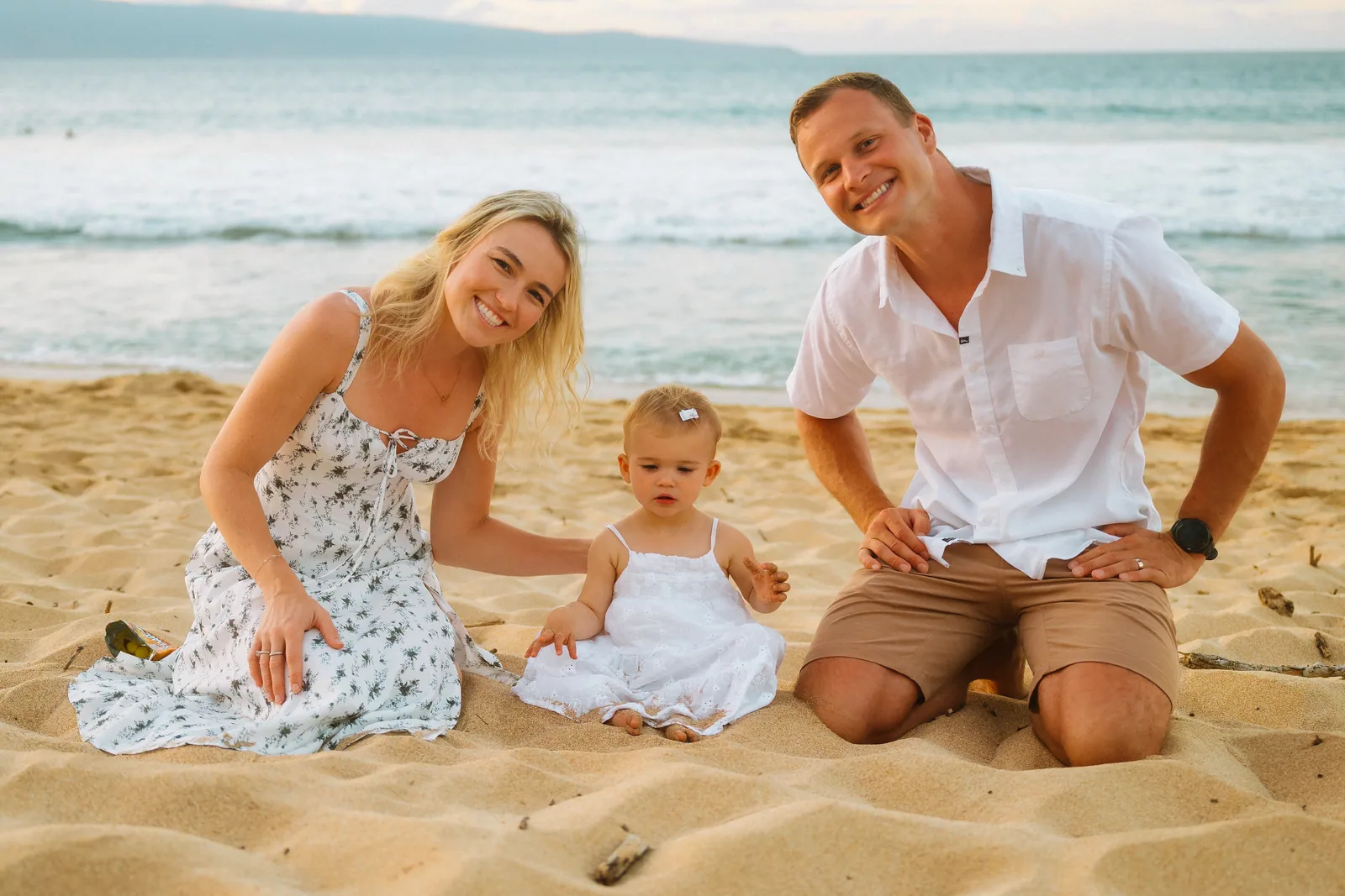 Parents kneeling in the sand beside their baby daughter