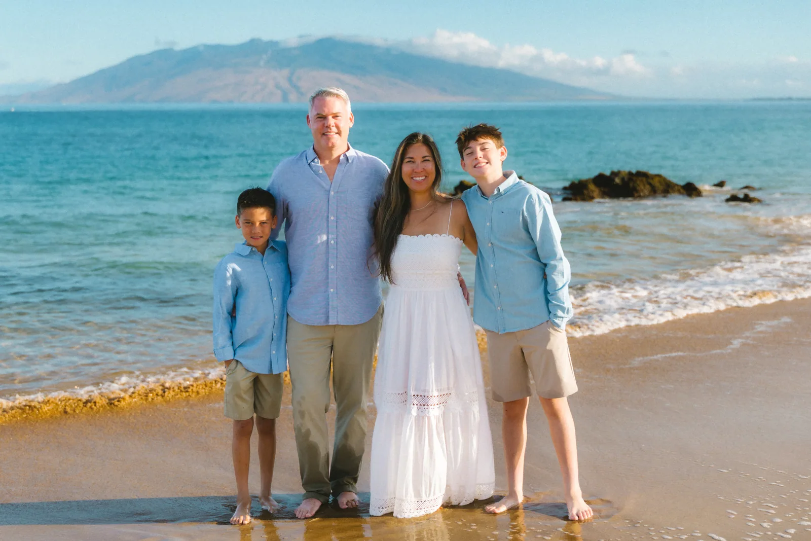 A family of four standing in the shallows with the mountains across the channel behind them