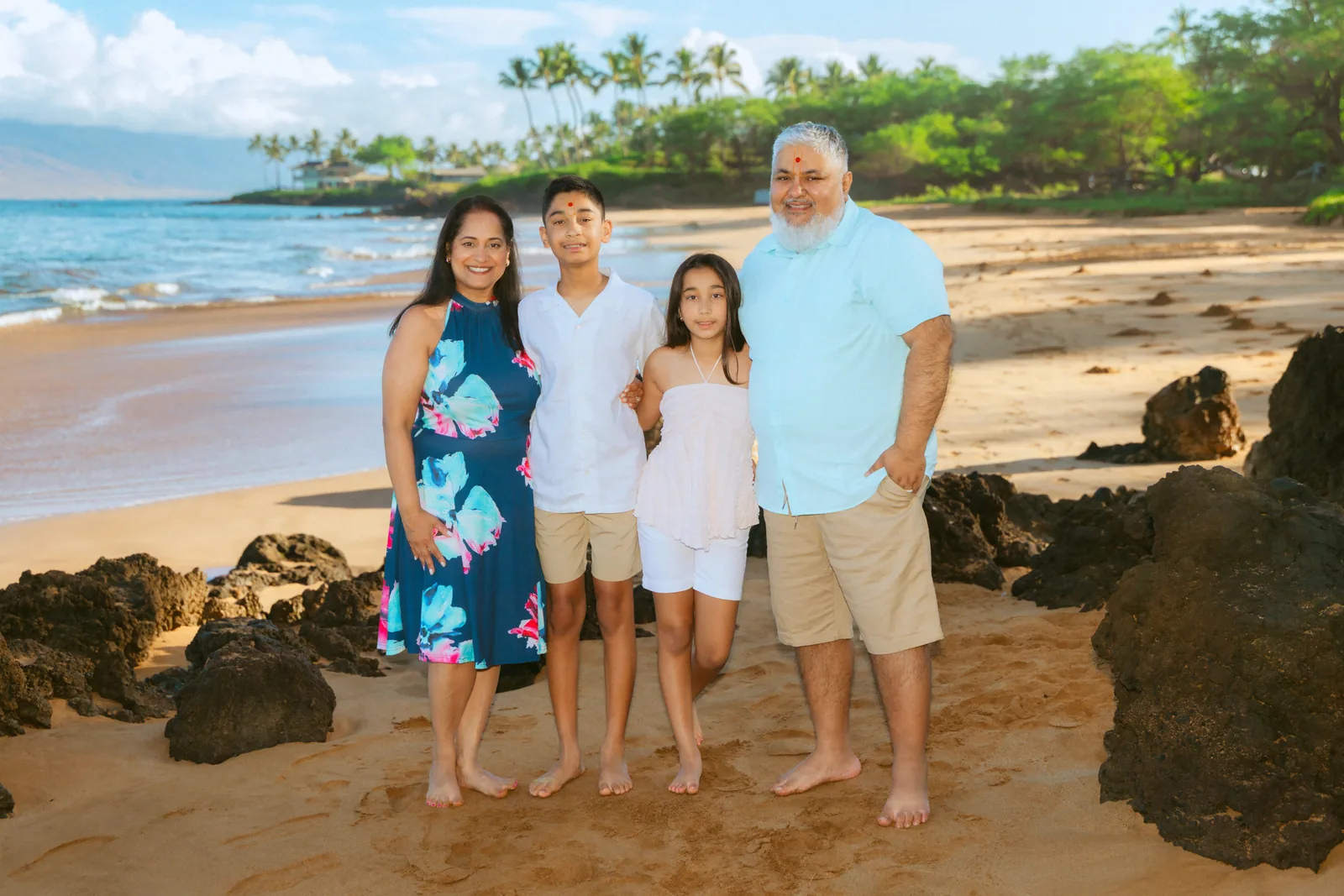 A family photographed among lava rocks with bright blue water behind