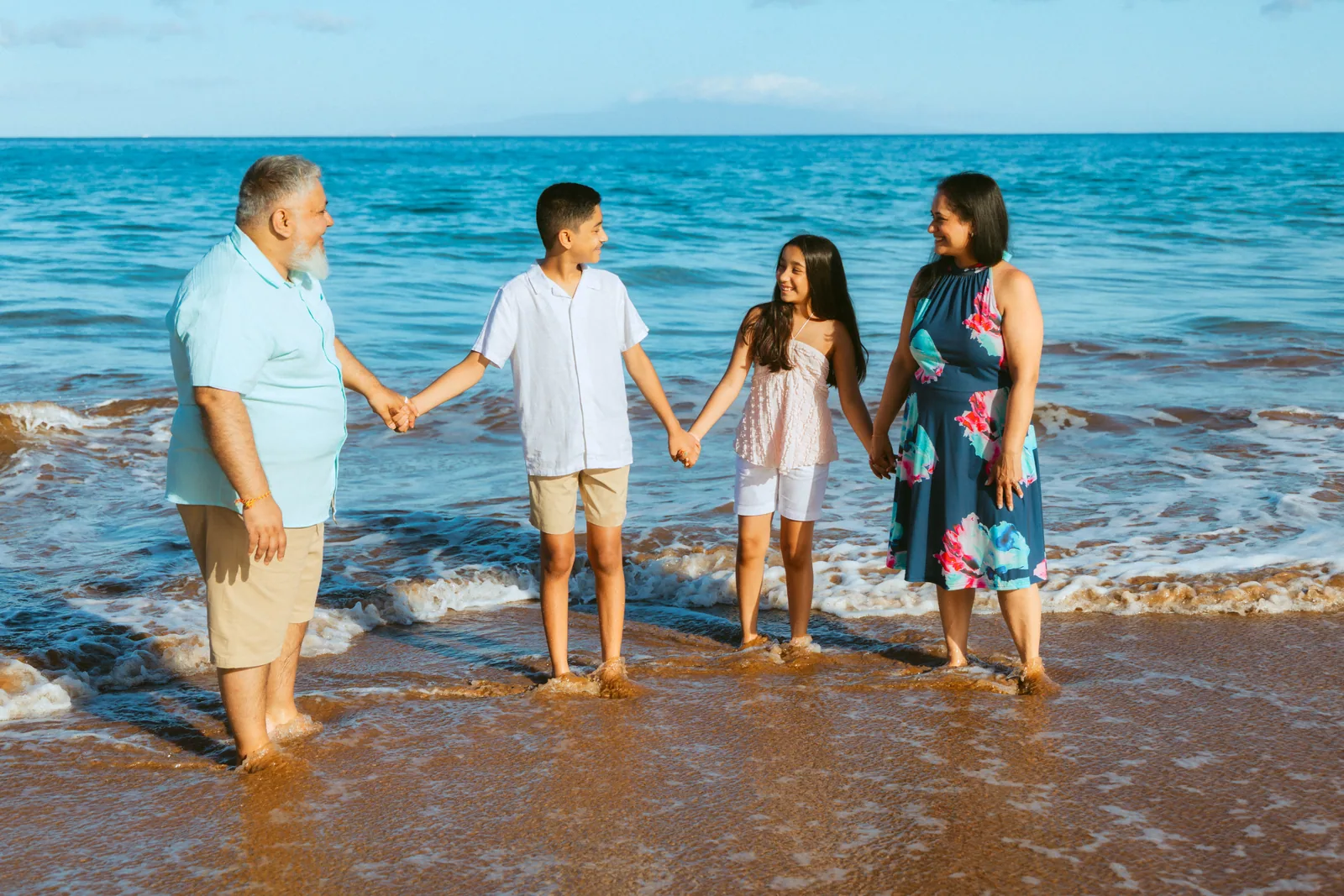 A family standing hand in hand in the shallows, facing the camera