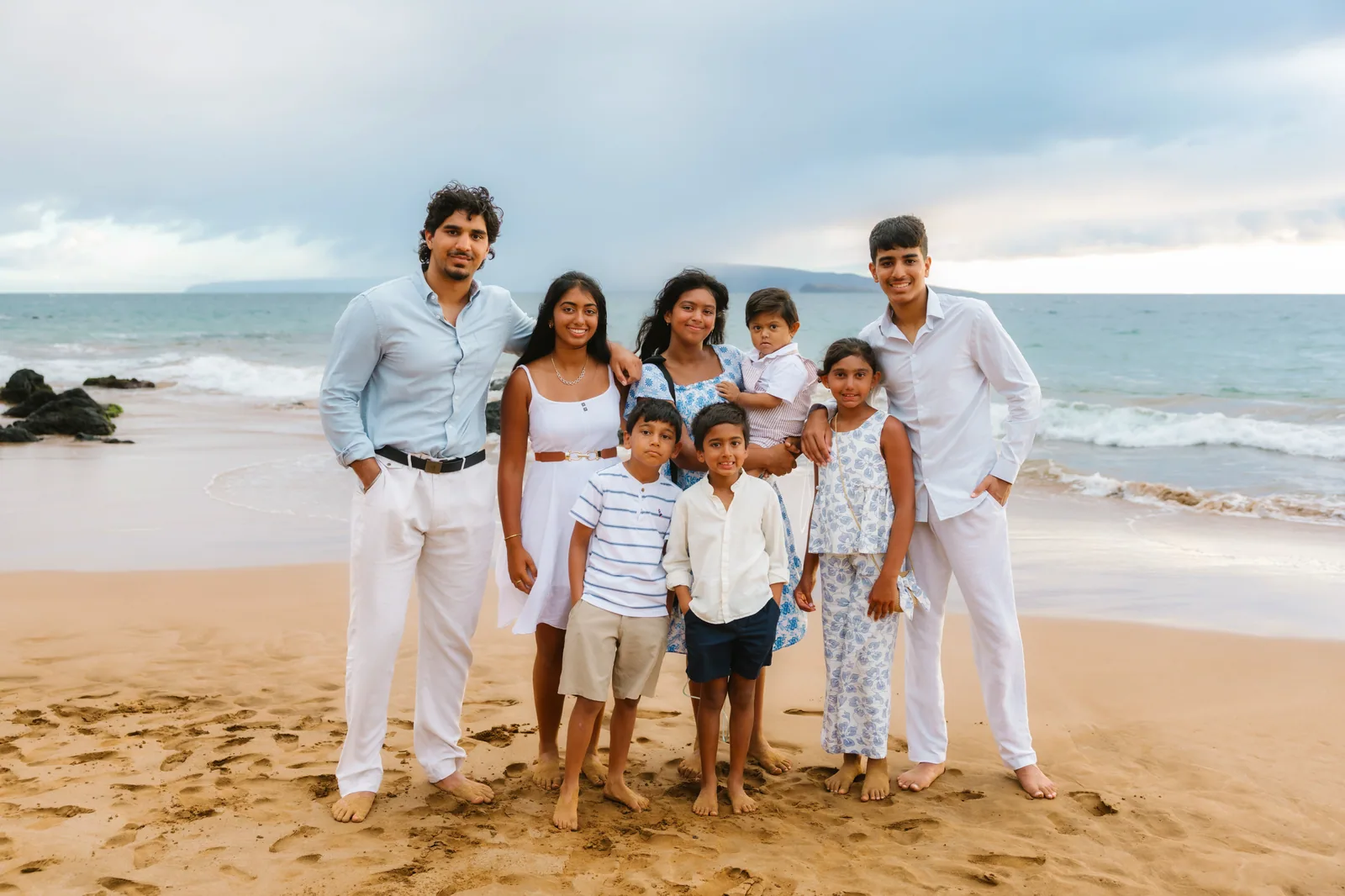 A large family group photographed together on the beach at golden hour