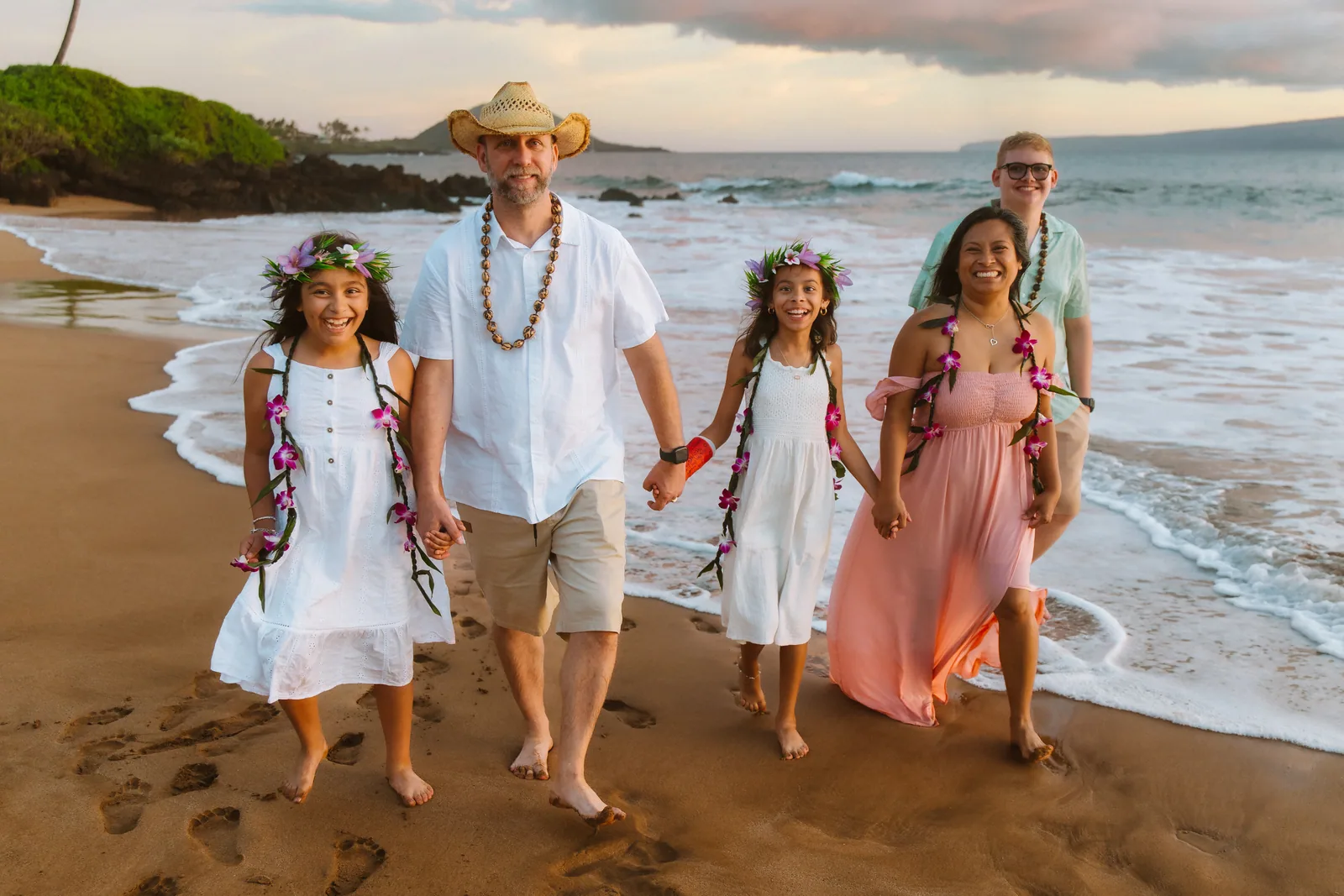 A family in leis and flower crowns walking the shoreline together
