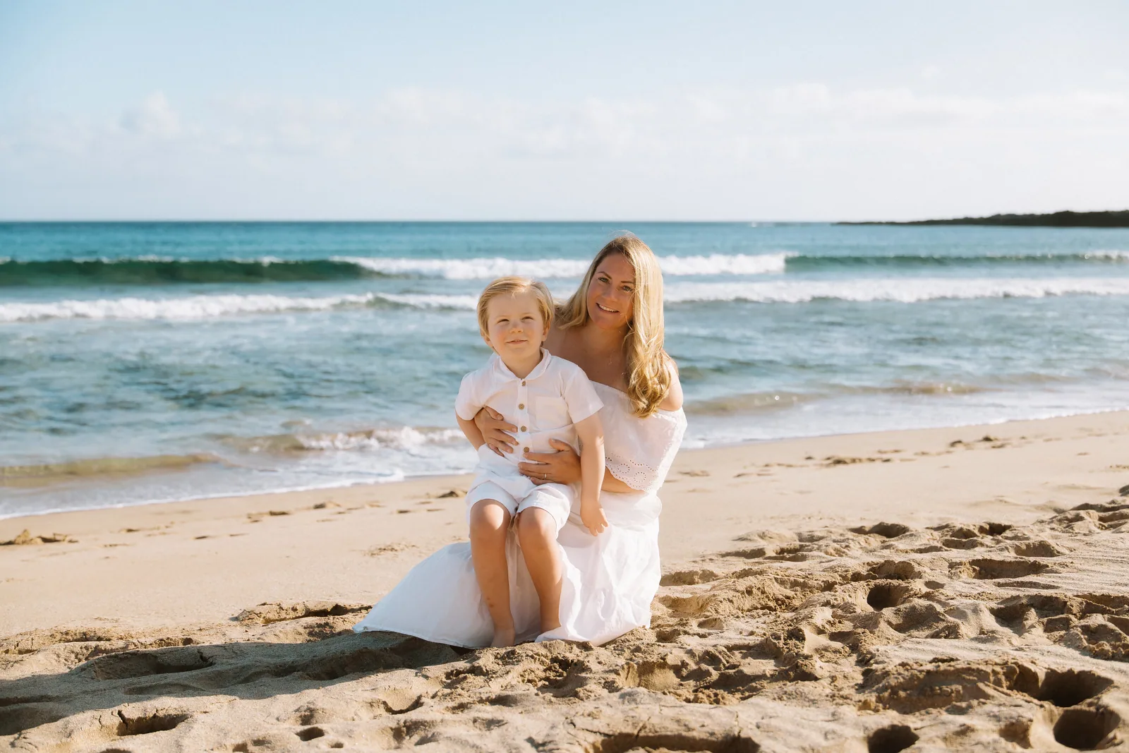 A mother and her young son sitting together on the sand
