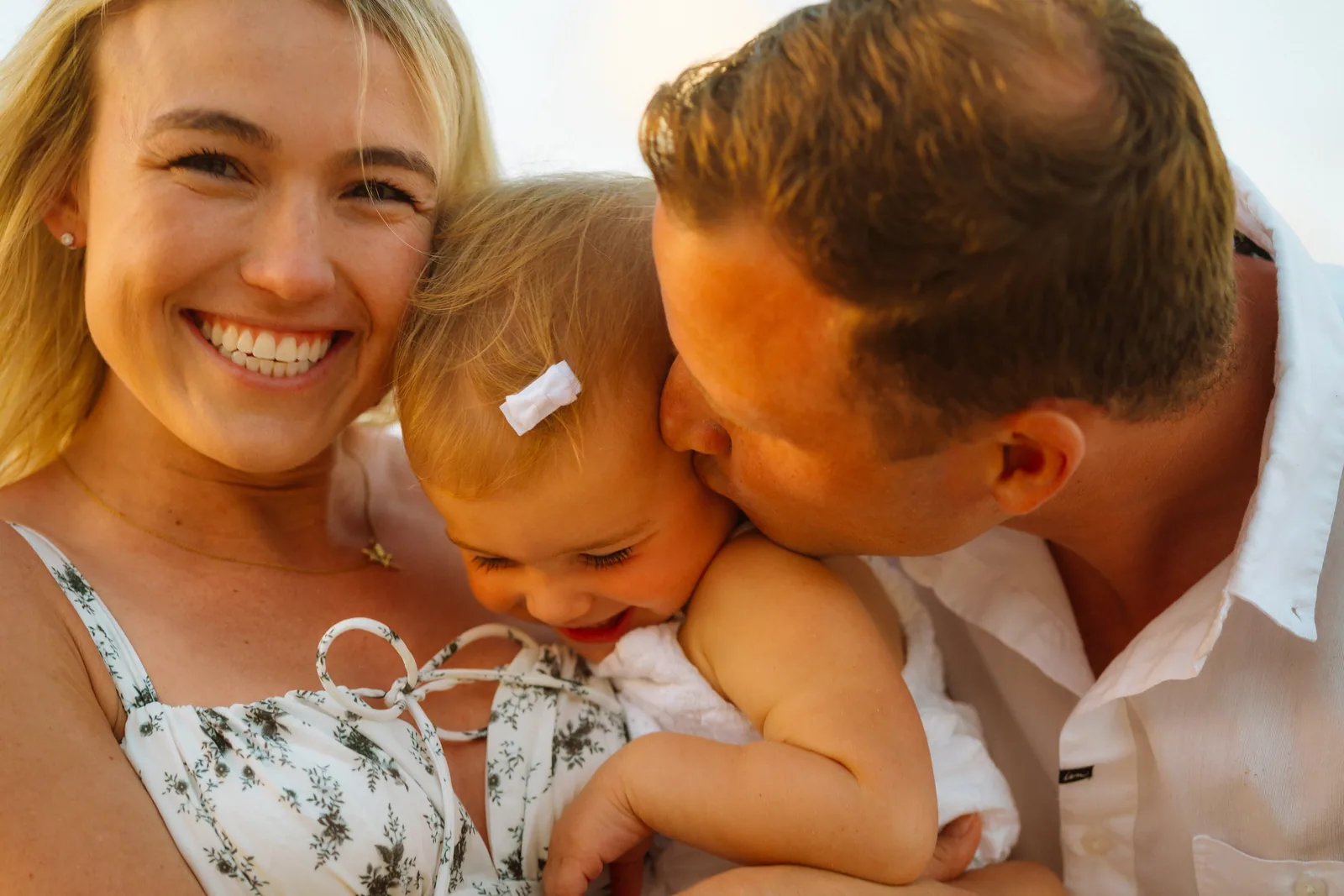 Parents kissing their baby between them in warm evening light