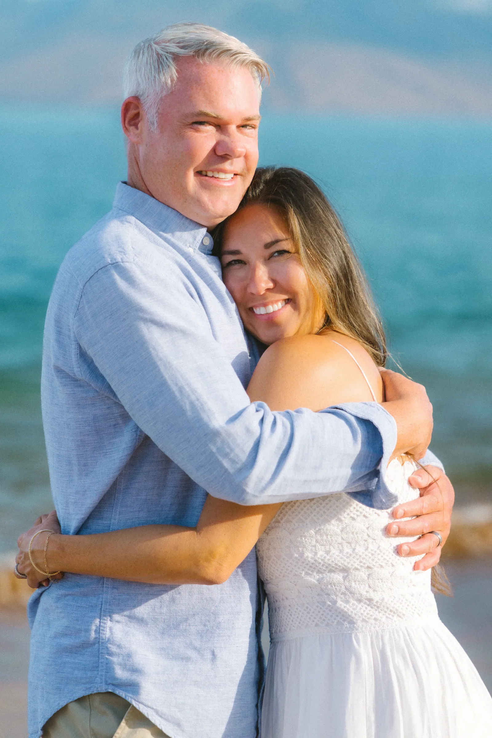 Two parents holding each other on the shoreline, laughing