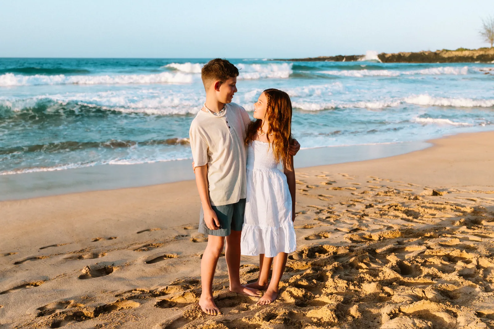 A brother and sister holding onto each other on the sand