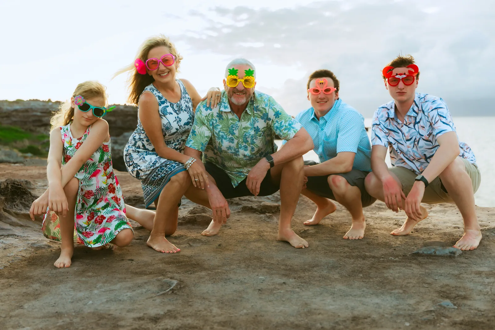 A family in matching aloha wear and novelty sunglasses on the rocks