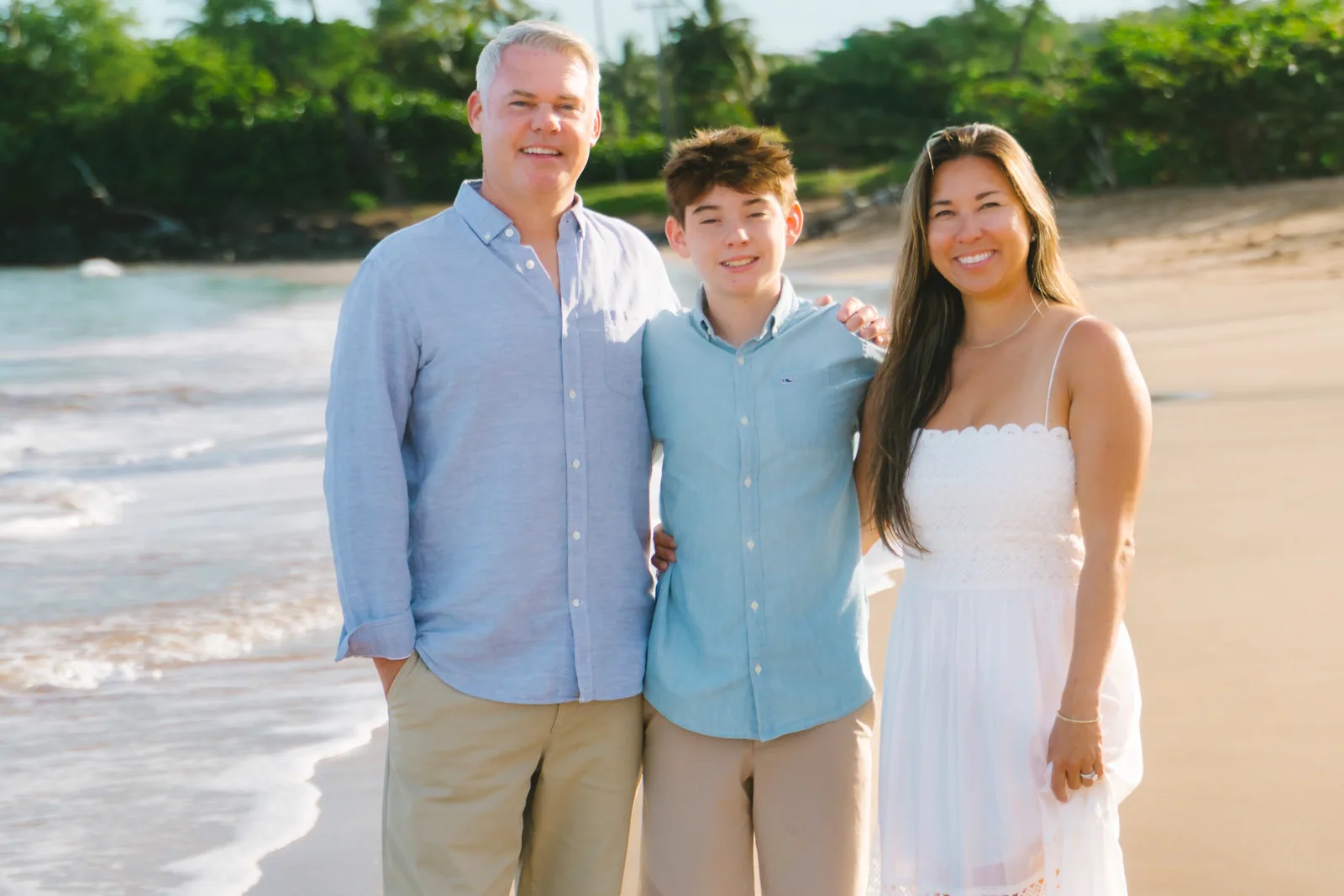 A family of three standing together in the shallows in blue and white