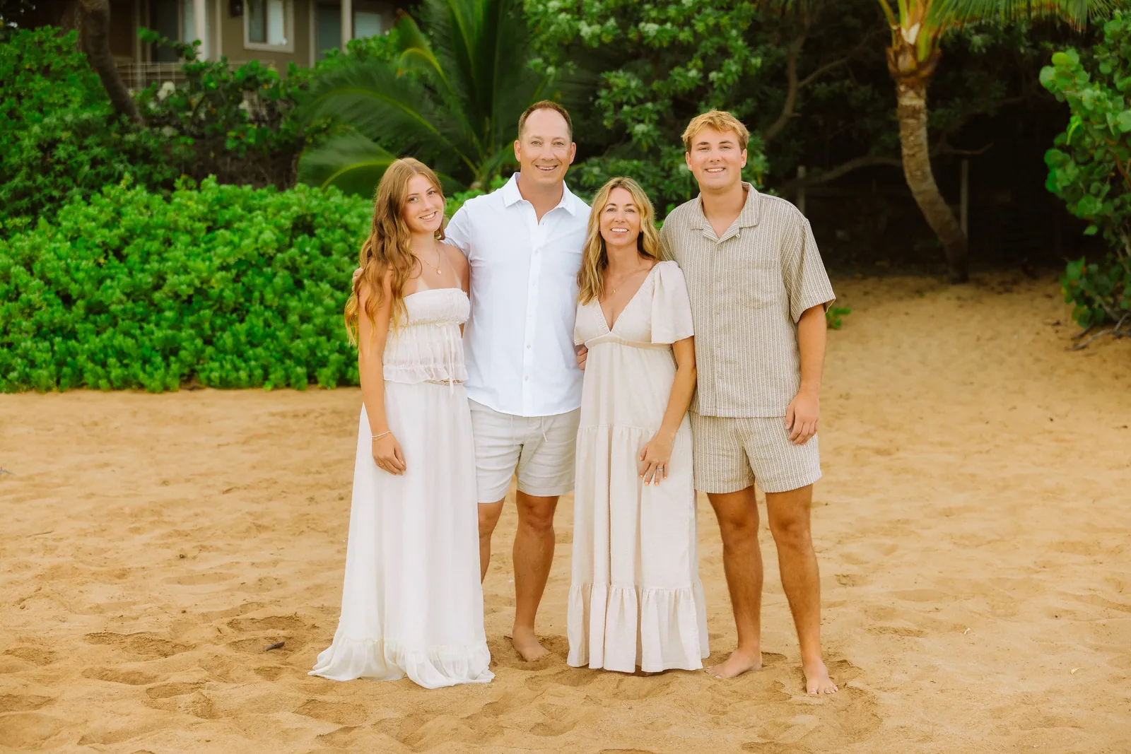 A family in white linen photographed under palms at the top of the beach