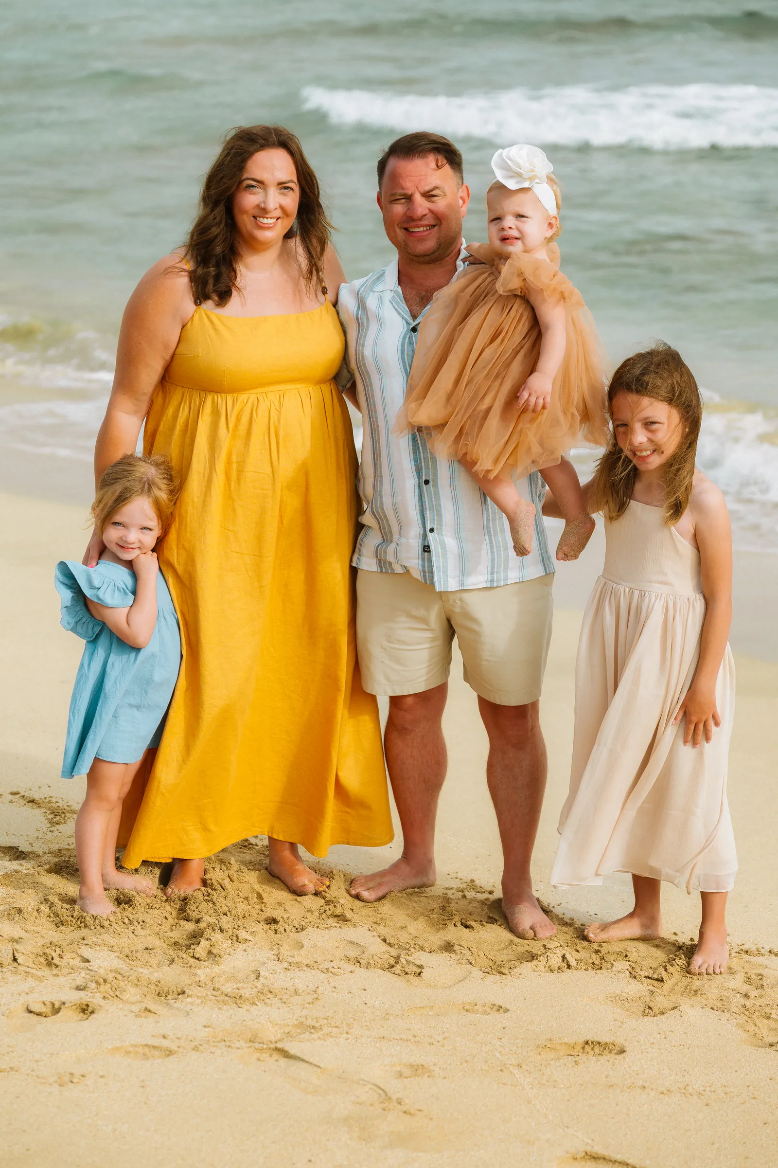 A family of six photographed together on the sand, the mother in yellow
