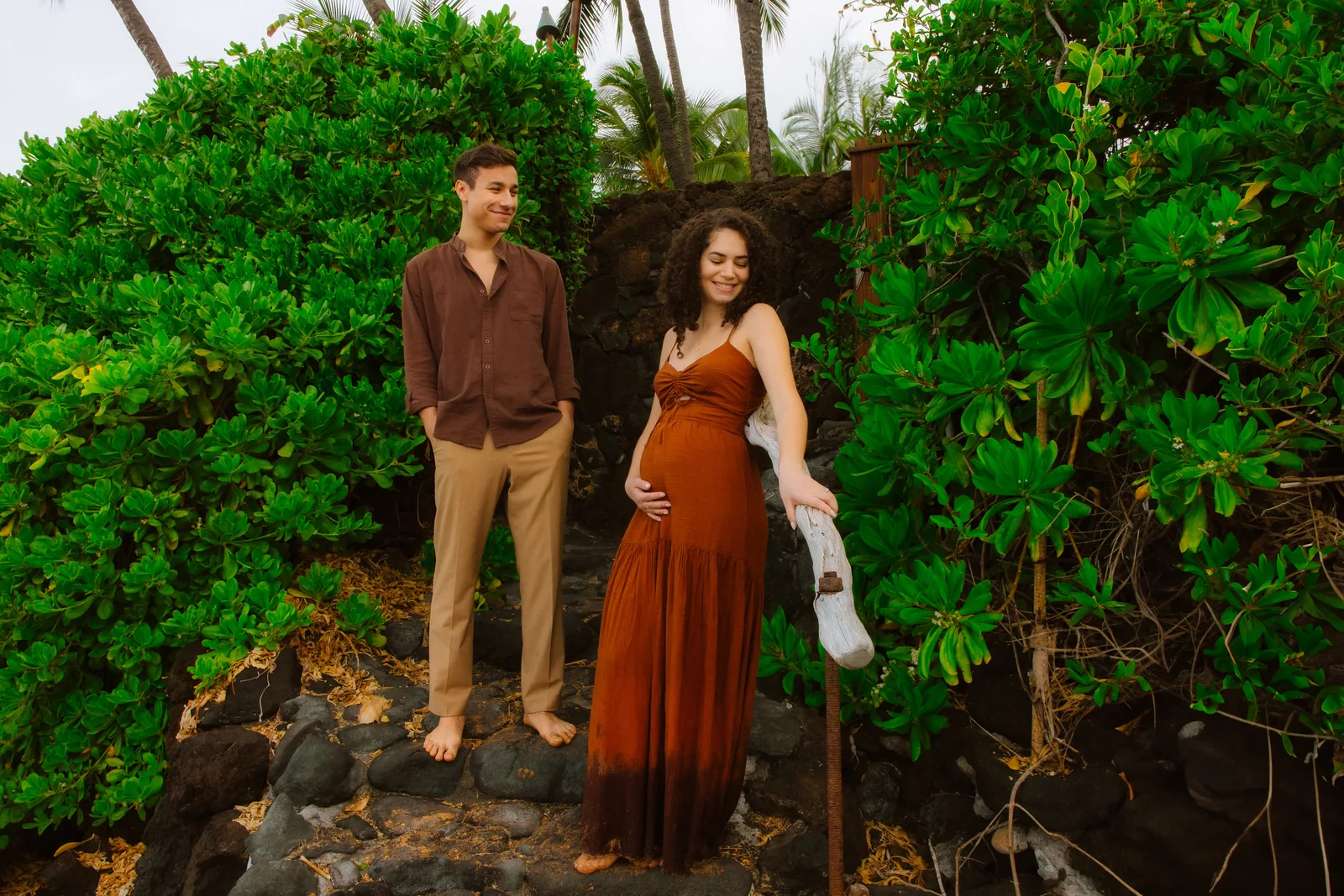 An expectant couple standing against dense green coastal growth