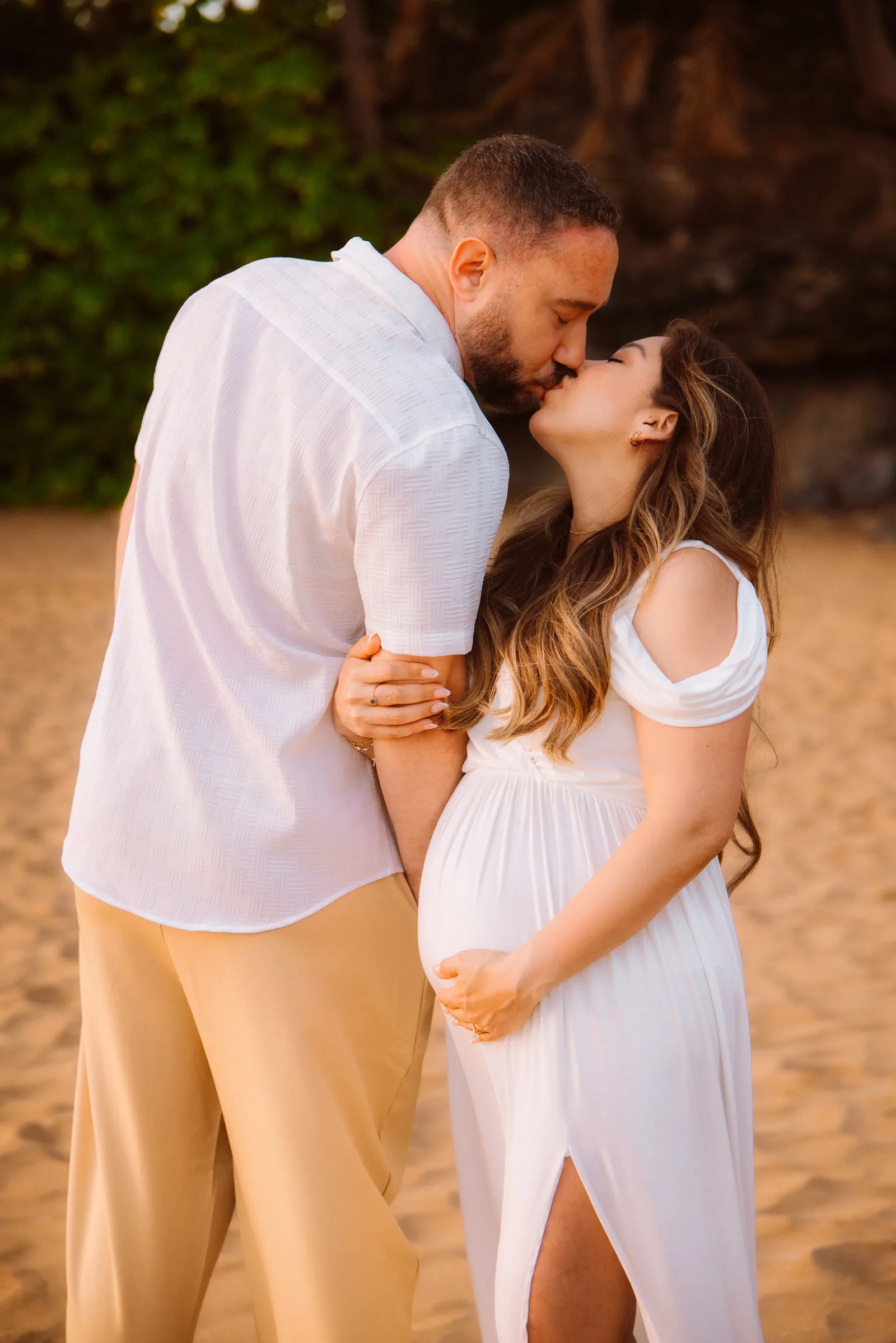 An expectant couple kissing beneath the palms