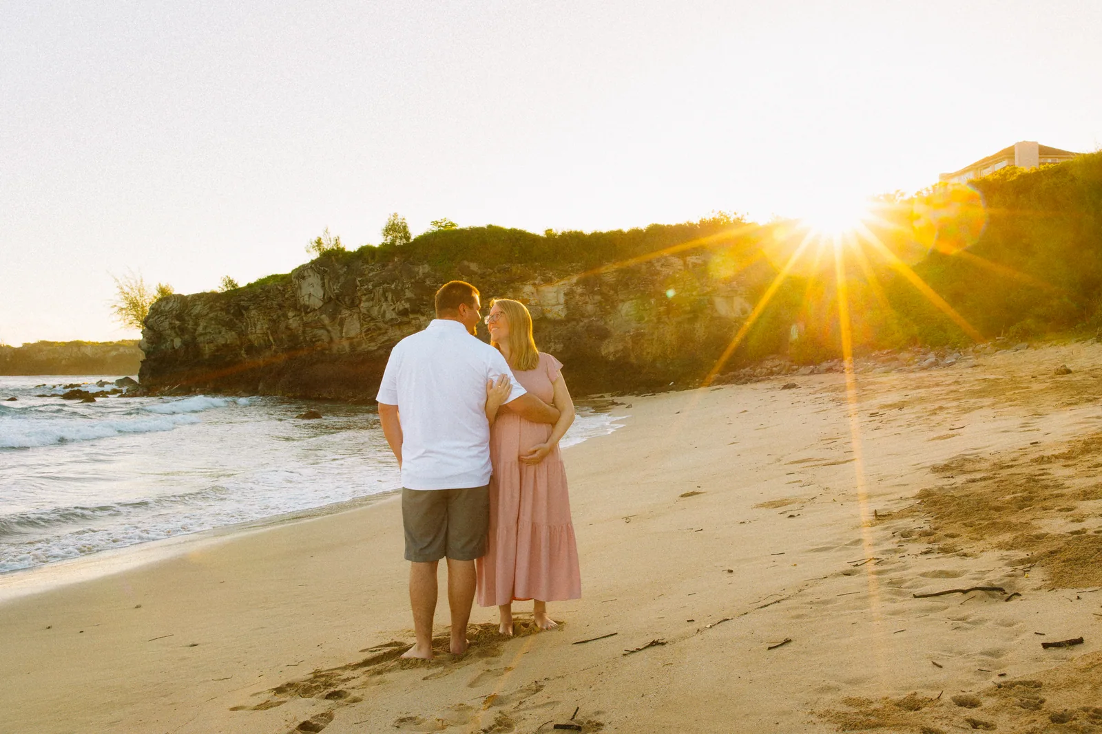 An expectant couple on the sand with the sun low behind them
