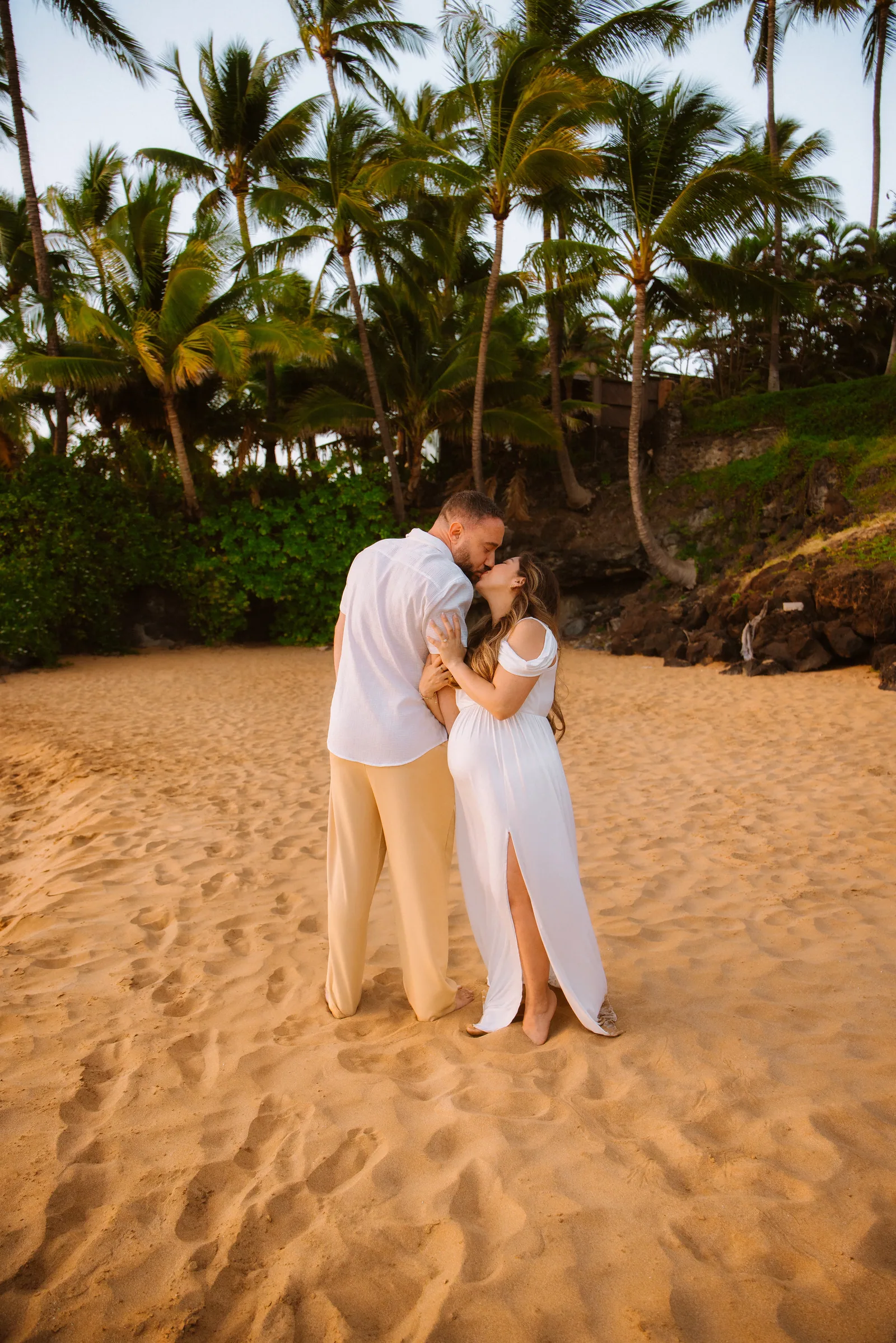 An expectant couple under palms, photographed from down the beach
