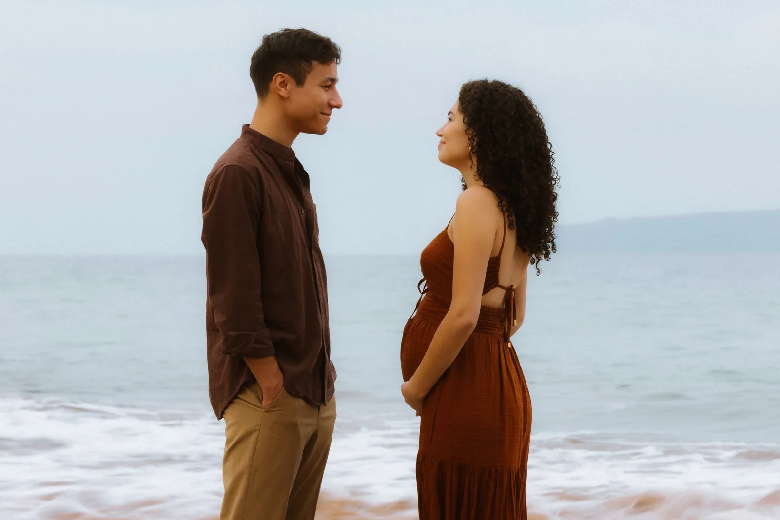 An expectant couple facing each other at the water's edge
