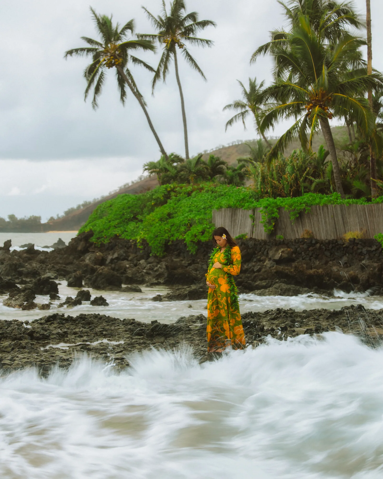 An expectant mother in a floral gown standing in the shorebreak