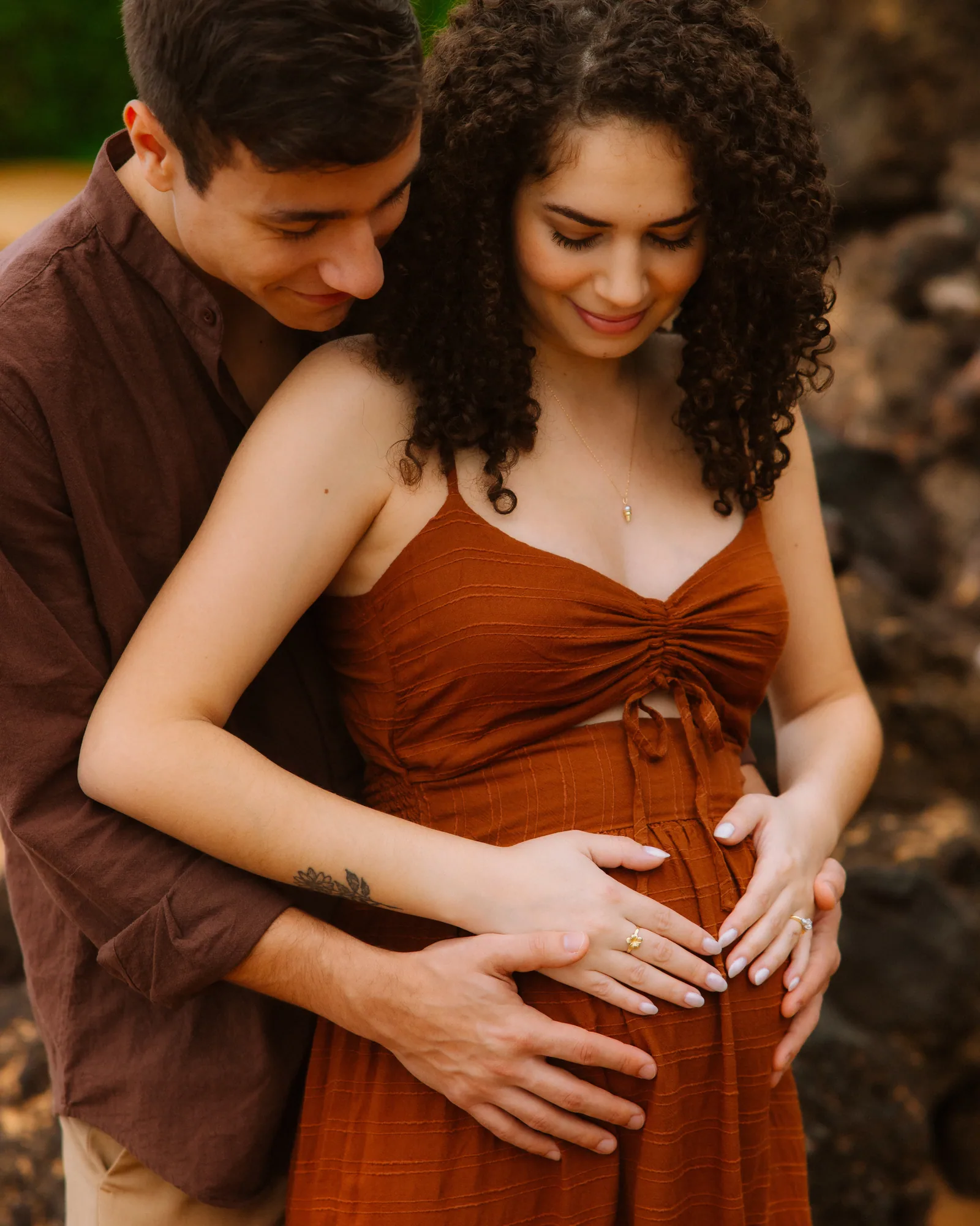 A partner's hands cradling the bump, close, in a rust dress