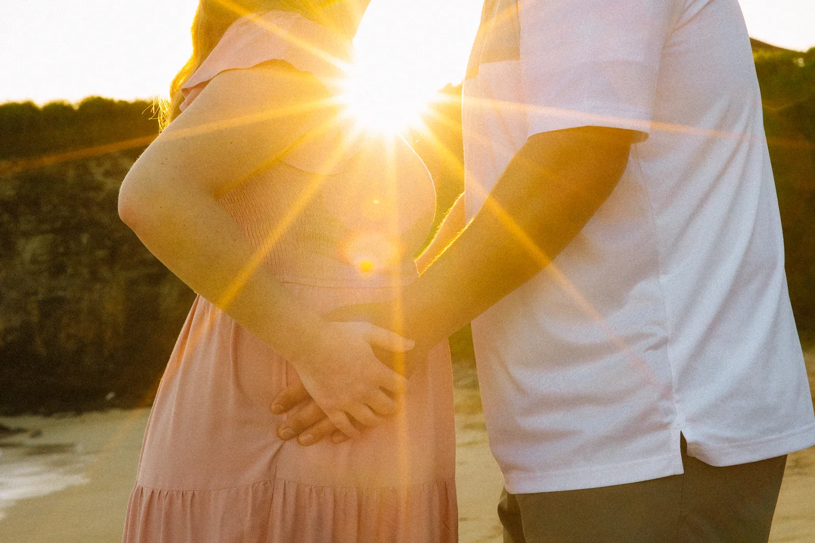 Both sets of hands on the bump with the sun flaring between them