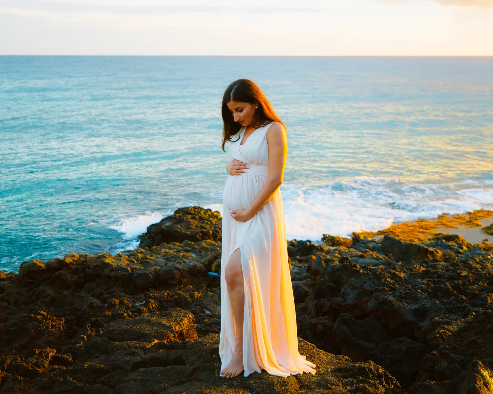 An expectant mother on lava rock above turquoise water