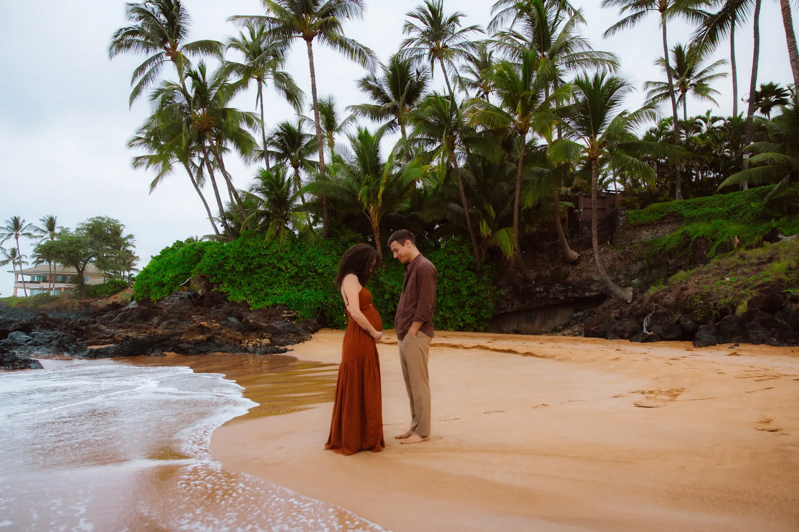An expectant couple on the sand beneath palms, photographed from a distance