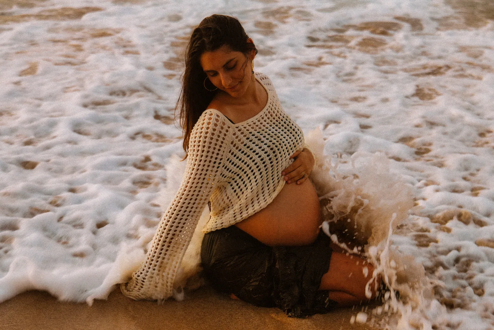 An expectant mother seated as the surf washes in around her