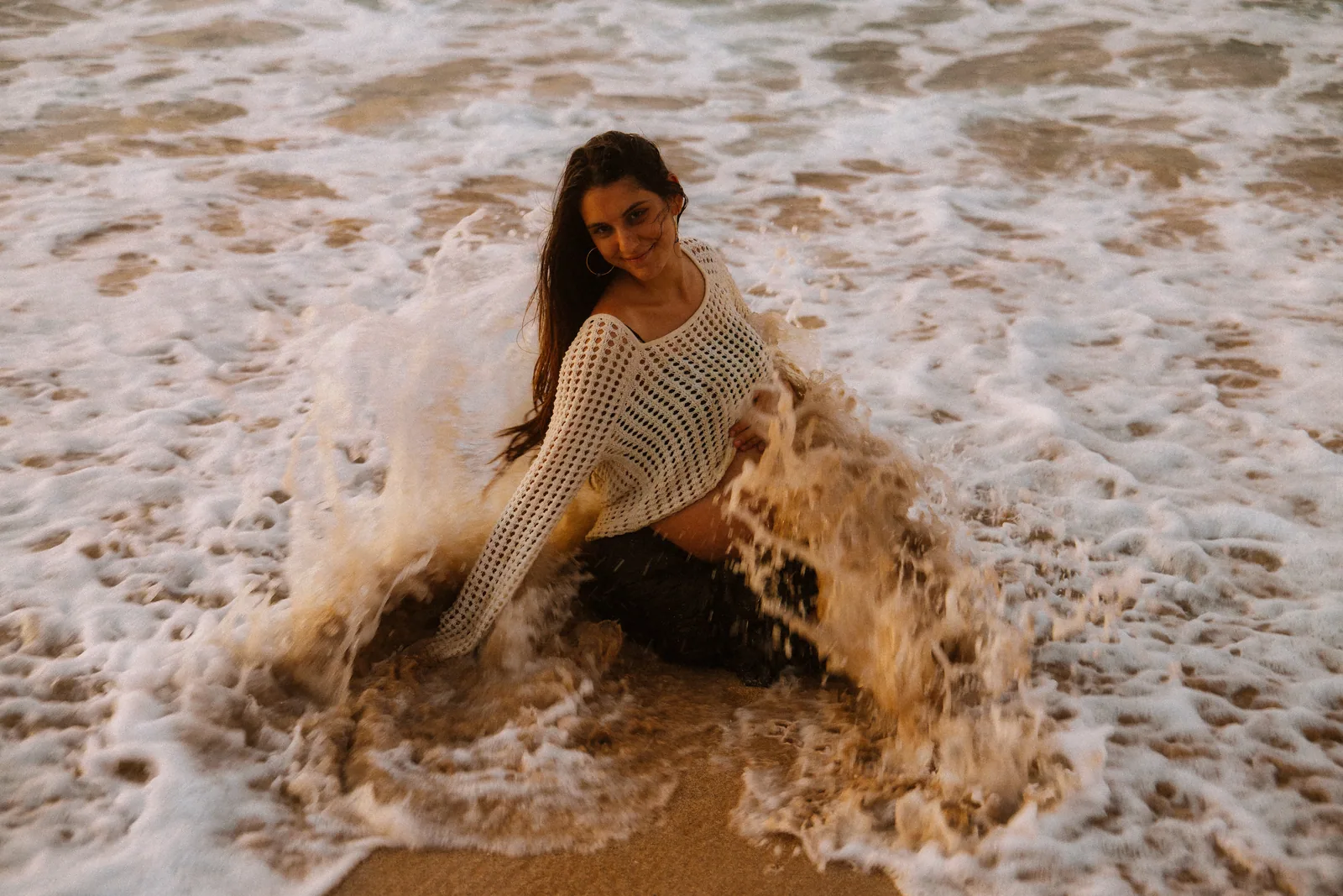 An expectant mother in the shorebreak with foam breaking around her