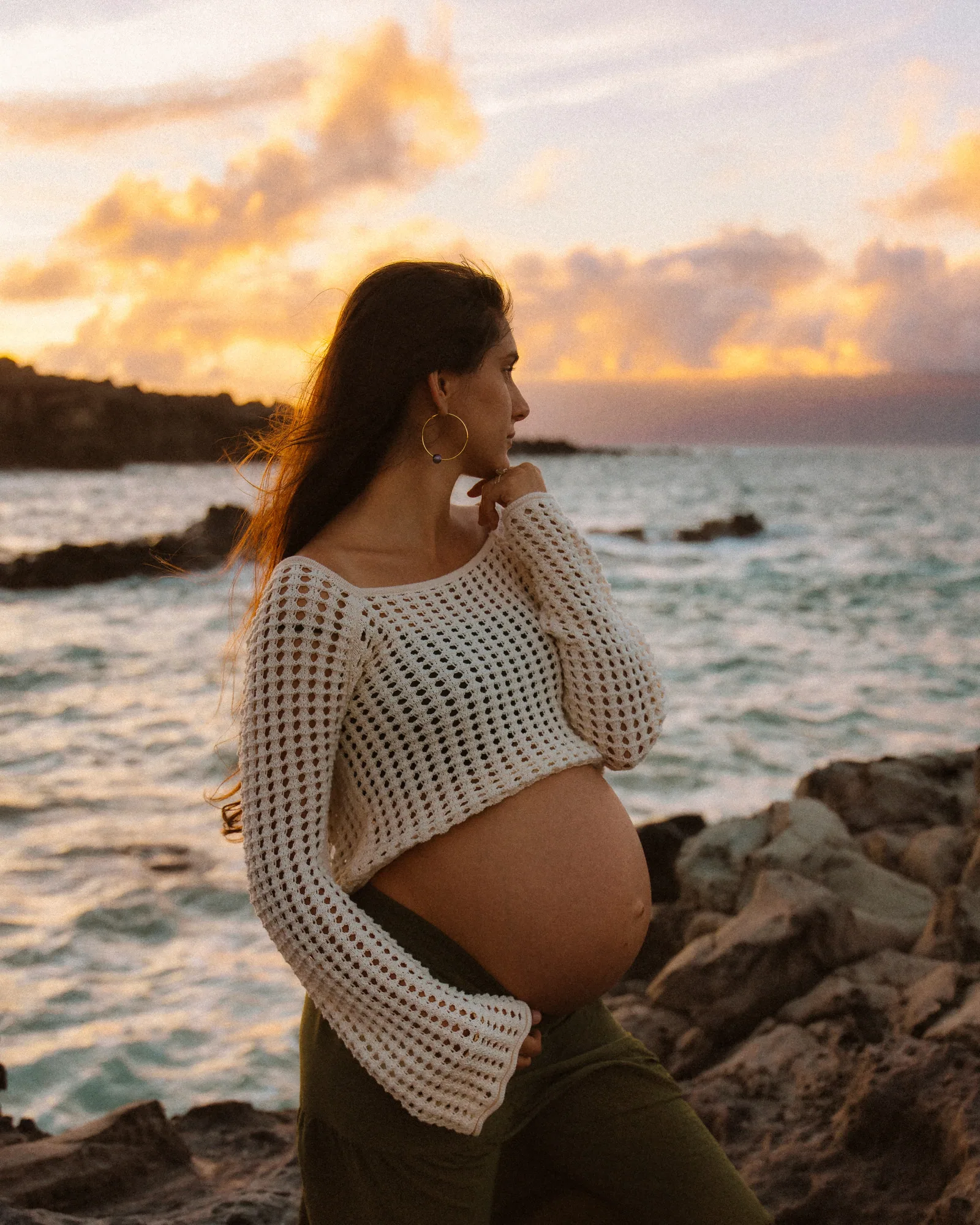 An expectant mother at sunset with her hands beneath the bump