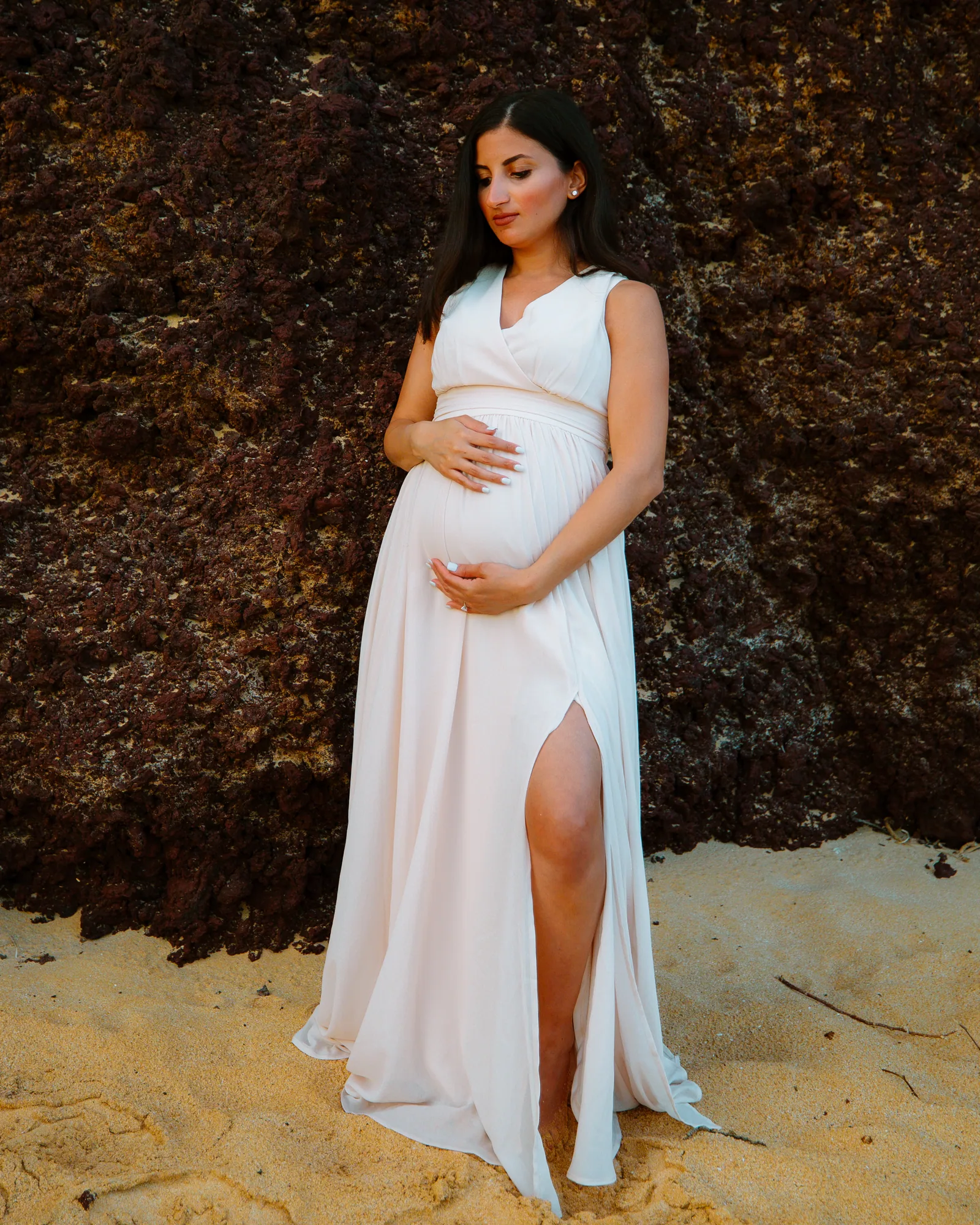 An expectant mother in a white gown against dark lava rock