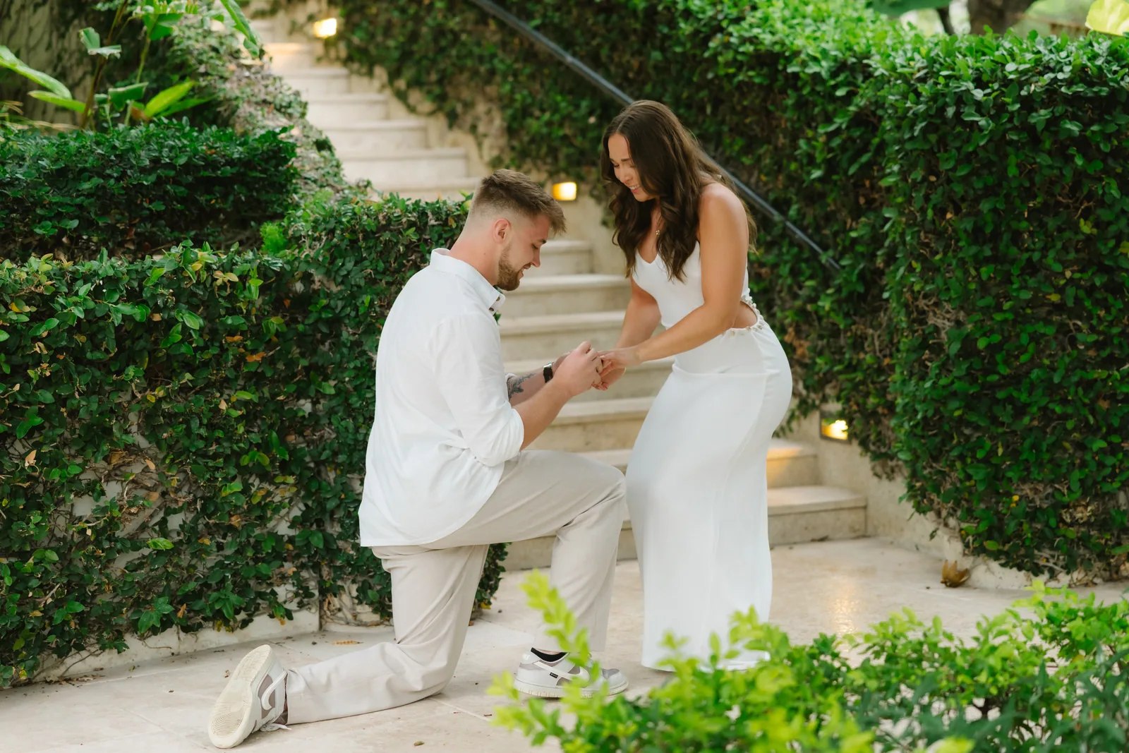 The ring box open between them on a hedged garden staircase