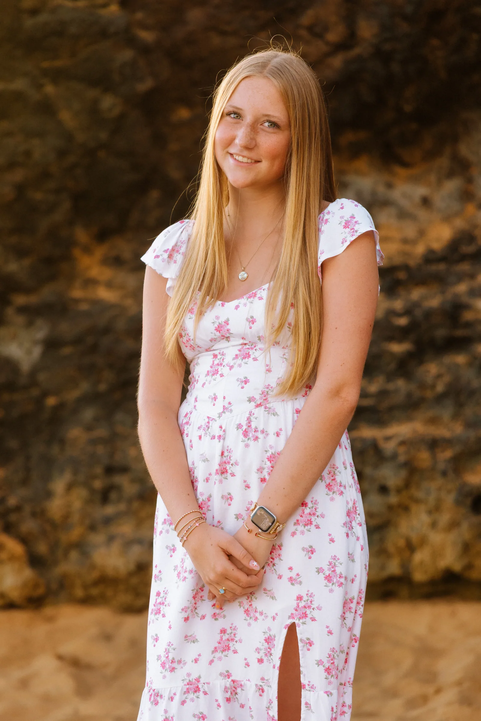 A senior portrait against dark lava rock, in a floral dress