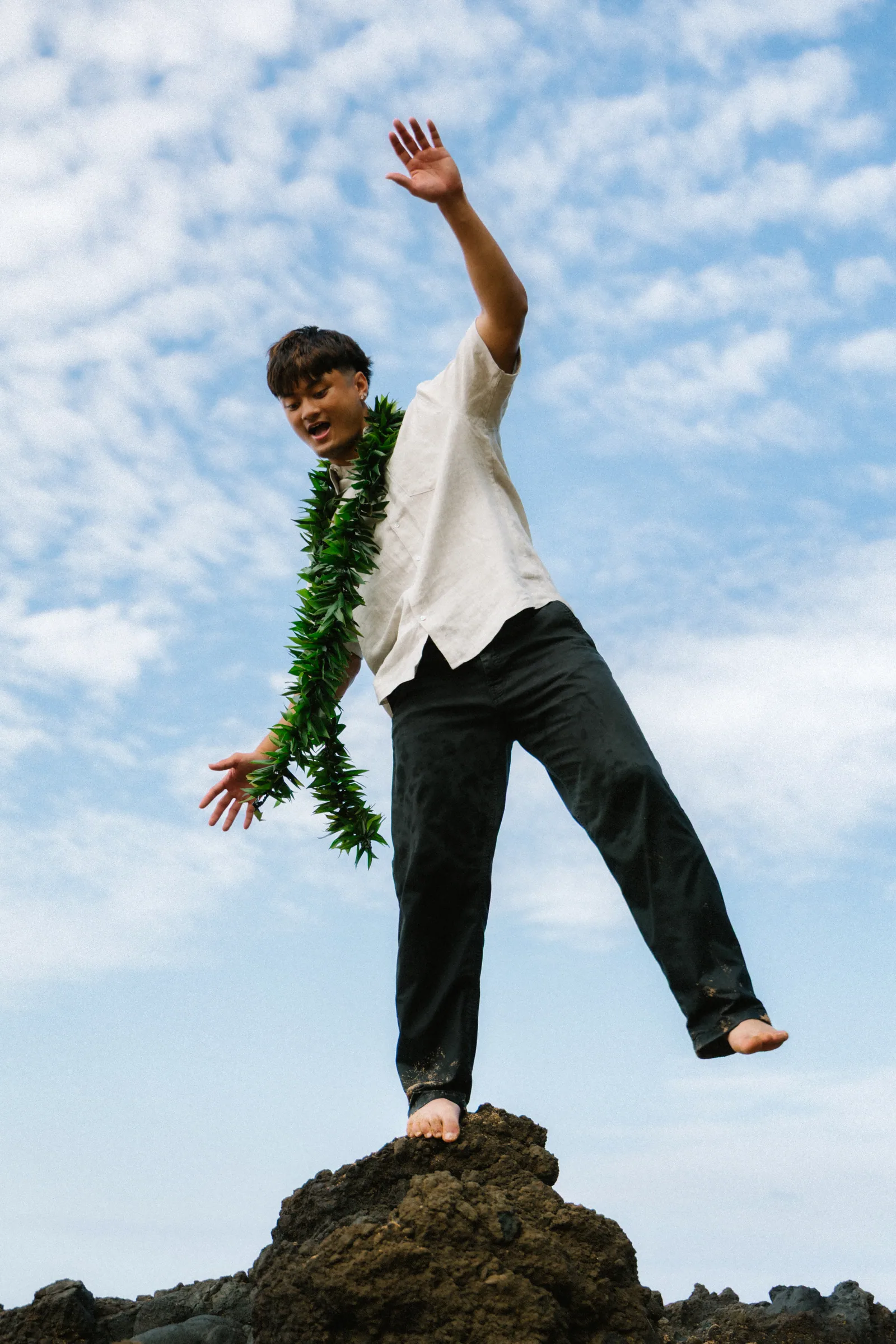 A senior portrait mid-jump from a lava rock, lei flying