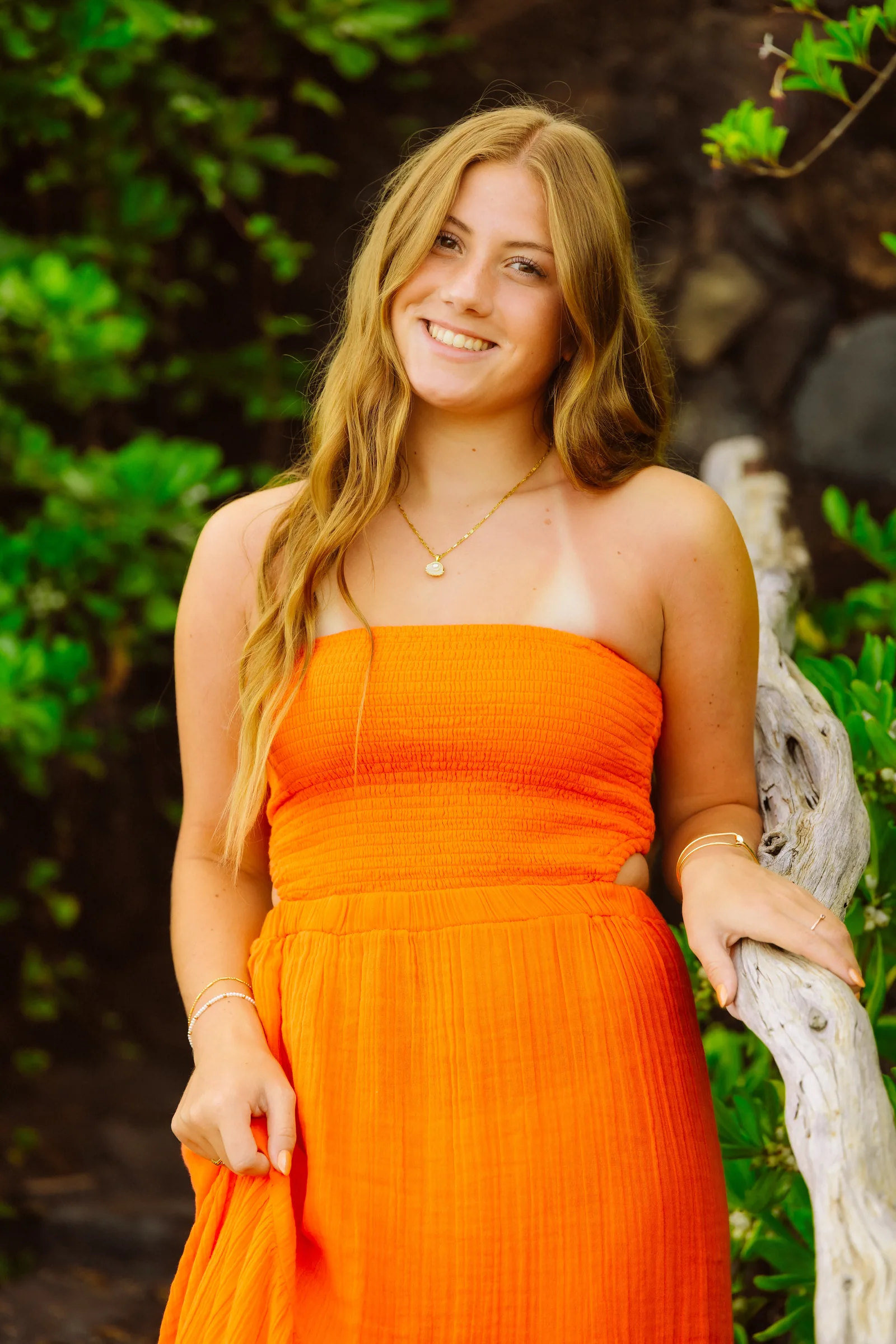 A senior portrait in an orange dress beside weathered driftwood